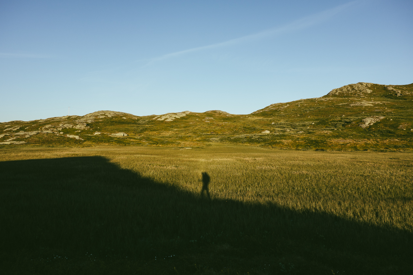 Luisa's shadow wearing a backback is visible in front of some lower mountains in the evening sun